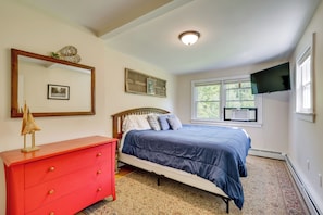 A bedroom with a bed, a dresser, a mirror, a television, and a window with an air conditioner. - Welcome to Buck's Hideout in Bridgton Maine! (Bridgton)
