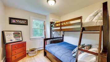 Una cama litera con colchón azul, un aparador de madera con cajones, recuerdos deportivos enmarcados y una ventana con vista a la vegetación.