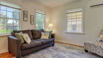 A living room with a gray sofa, patterned armchair, and a large window with blinds.