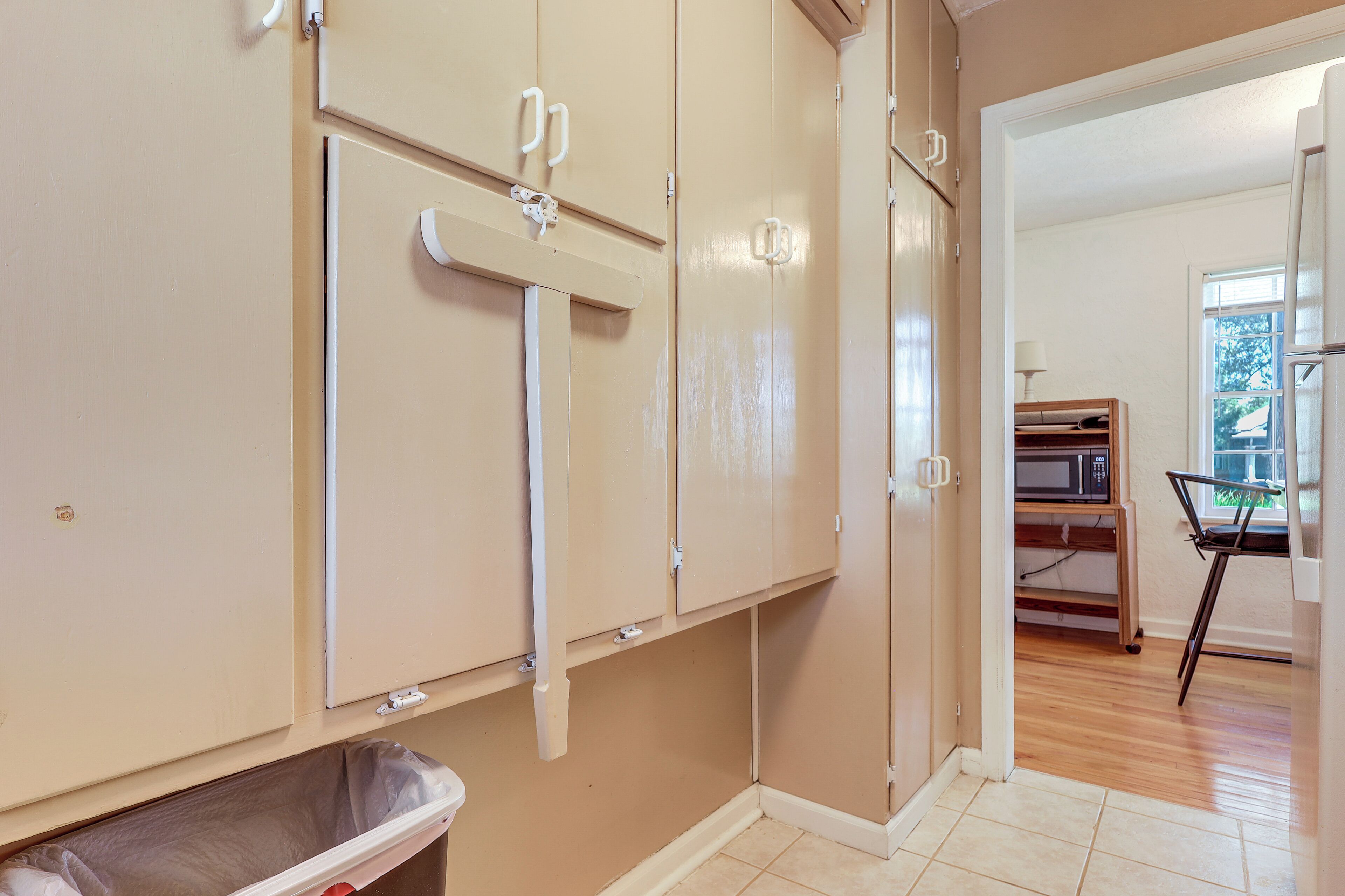 A room with beige walls, a trash bin, and a microwave on a shelf.
