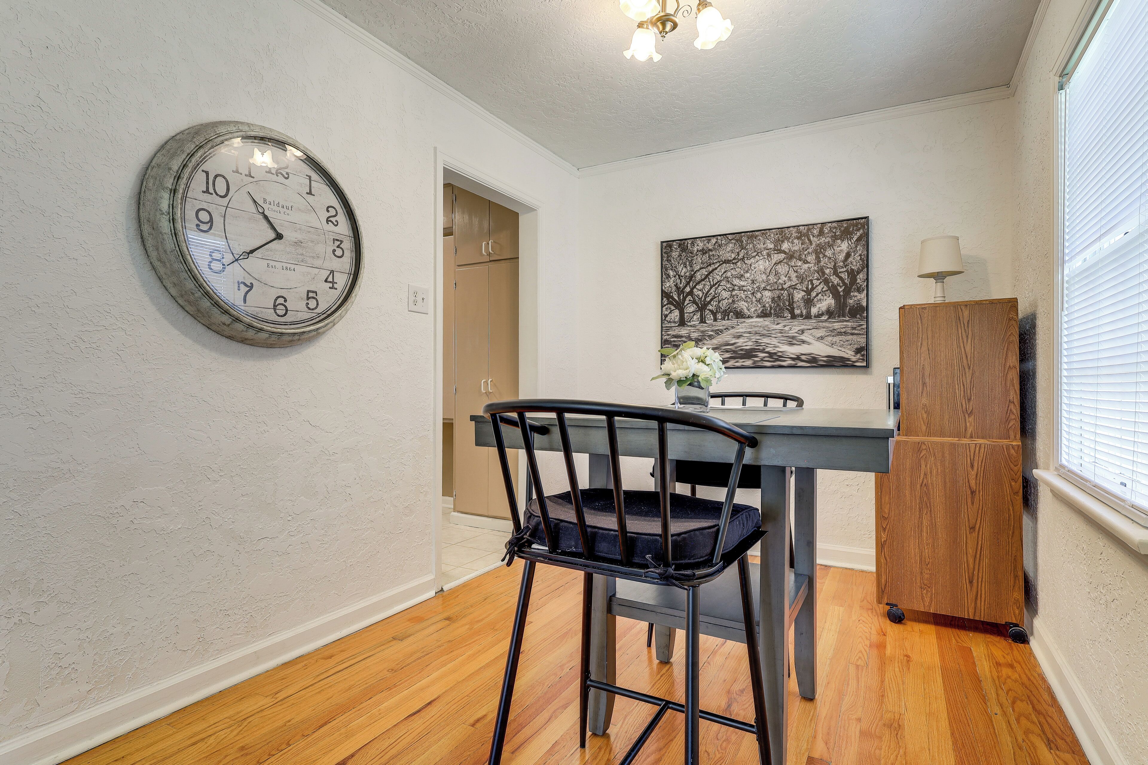 A dining area with a wooden table, a black chair, a clock, and a painting on the wall.