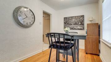 A dining area with a wooden table, a black chair, a clock, and a painting on the wall.