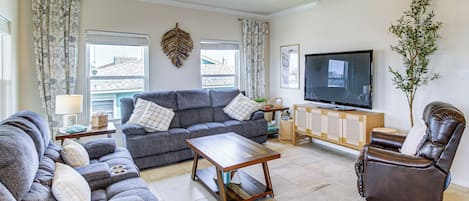 A living room with a grey sofa, a brown leather chair, a wooden coffee table, and a flat-screen TV on a wooden cabinet.