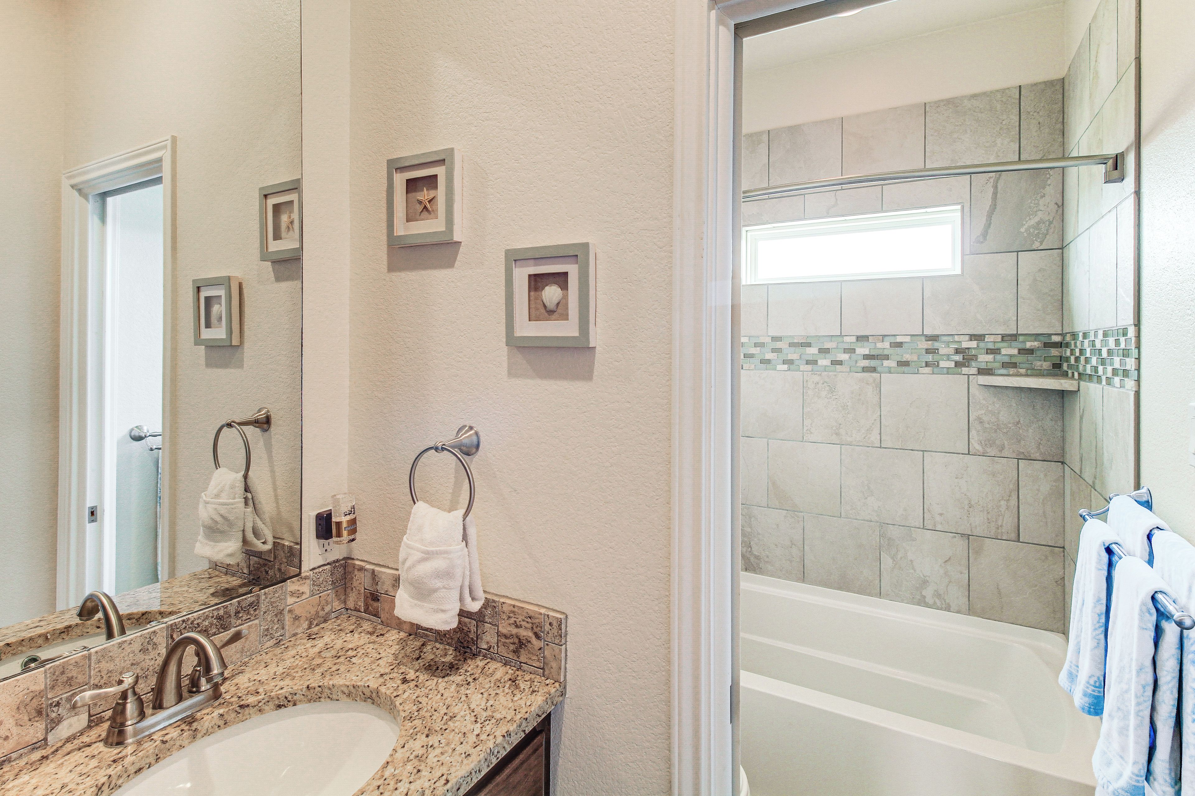 A bathroom with a granite countertop sink, a mirror, framed pictures on the wall, and a glass-enclosed shower area.