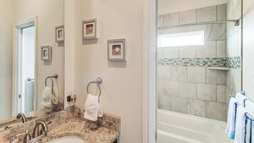 A bathroom with a granite countertop sink, a mirror, framed pictures on the wall, and a glass-enclosed shower area.