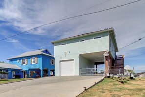 Un edificio de dos pisos con una puerta de garaje, una casa azul a la izquierda y un cielo despejado.