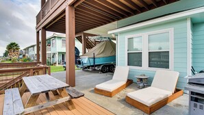 A covered deck with wooden furniture, a boat, and a house with a light blue exterior. - Waterfront Retreat w/ Dock in Rockport! (Rockport)