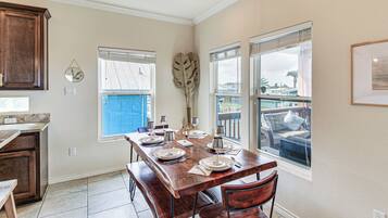A dining area with a wooden table set for four, a kitchen with dark wooden cabinets, and a view of a balcony with outdoor furniture.