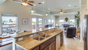 A spacious kitchen with granite countertops, a double sink, and a dining area with a gray sofa. - Waterfront Retreat w/ Dock in Rockport! (Rockport)