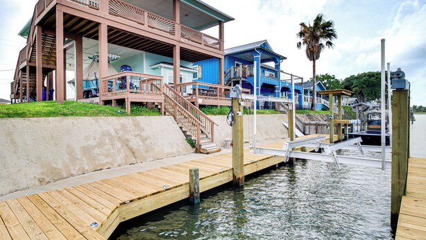 A waterfront property with a wooden dock, a covered area with stairs, and a blue building with a balcony. - Waterfront Retreat w/ Dock in Rockport! (Rockport)