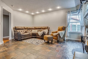 A corner living room with a sectional sofa, a single armchair, a patterned rug, and a large window with curtains. - Treehouse Views! Walking Distance to IMS (Indianapolis)