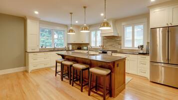 A modern kitchen with a central island, bar stools, stainless steel appliances, and pendant lighting.