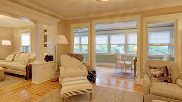 A spacious living room with a sofa, armchair, ottoman, and a chandelier.