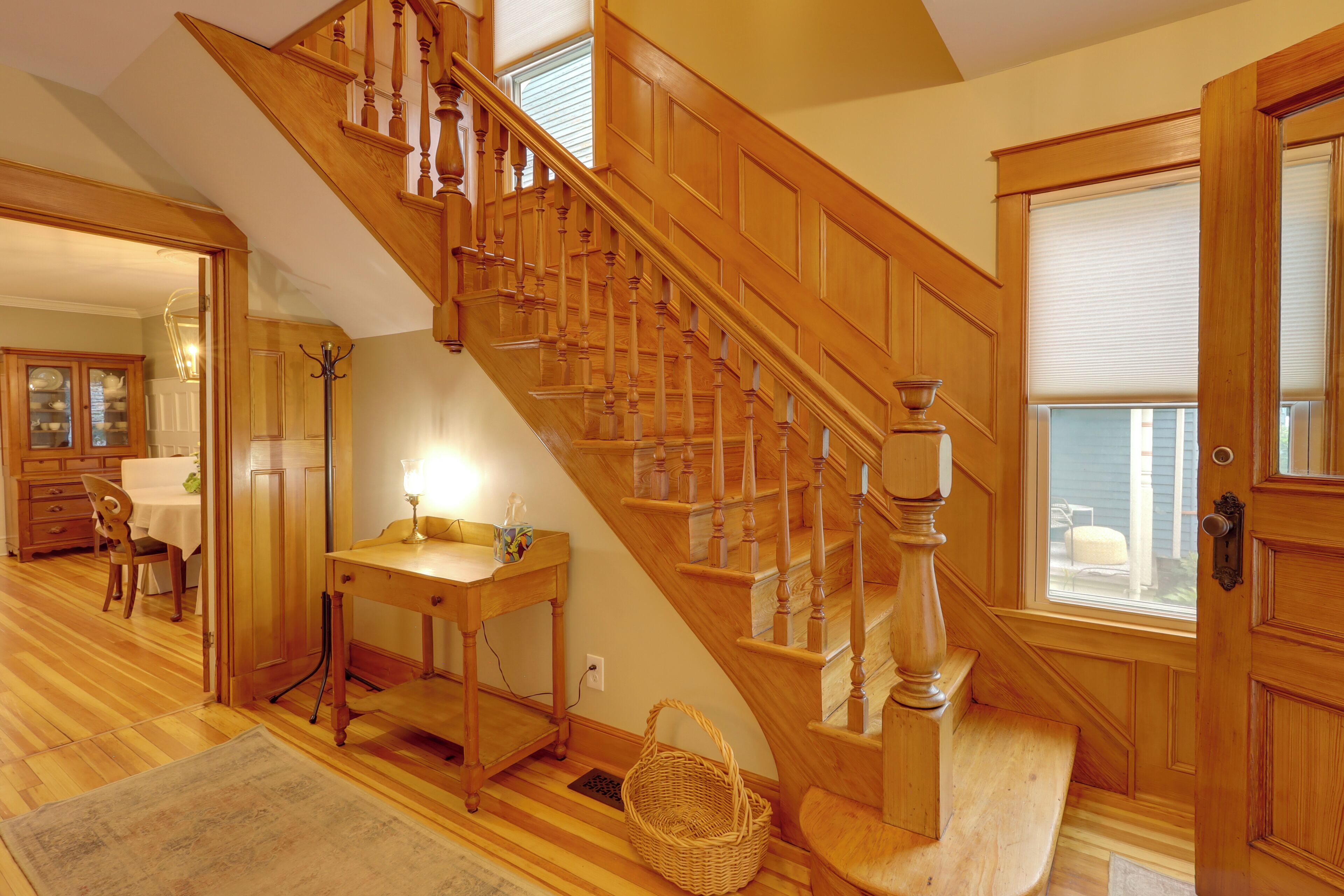 A wooden staircase with a handrail, a dining area with a table and chairs, and a door with a window.