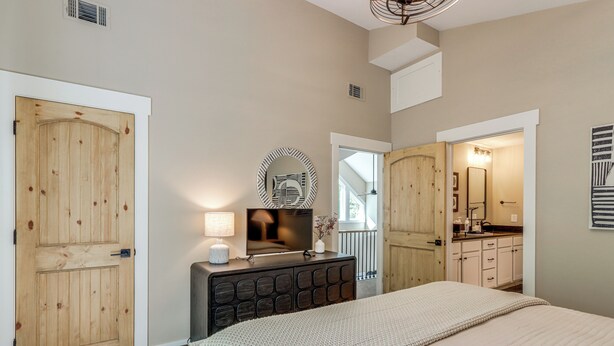 A bedroom with a large bed, a dresser, a television, and a bathroom visible through an open door. - Screened Porch + Home Office: Modern Ellijay Cabin (Ellijay)