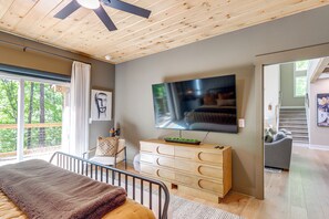 A modern bedroom with a bed, a dresser, a TV, and a view of the outdoors. - Screened Porch + Home Office: Modern Ellijay Cabin (Ellijay)