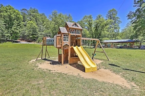 Ein hölzernes Spielhaus mit gelber Rutsche in einem grünen Park.