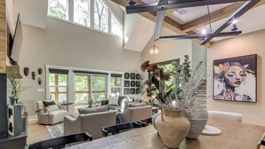 A spacious living area with a dining table, sofas, and a large window. - Screened Porch + Home Office: Modern Ellijay Cabin (Ellijay)