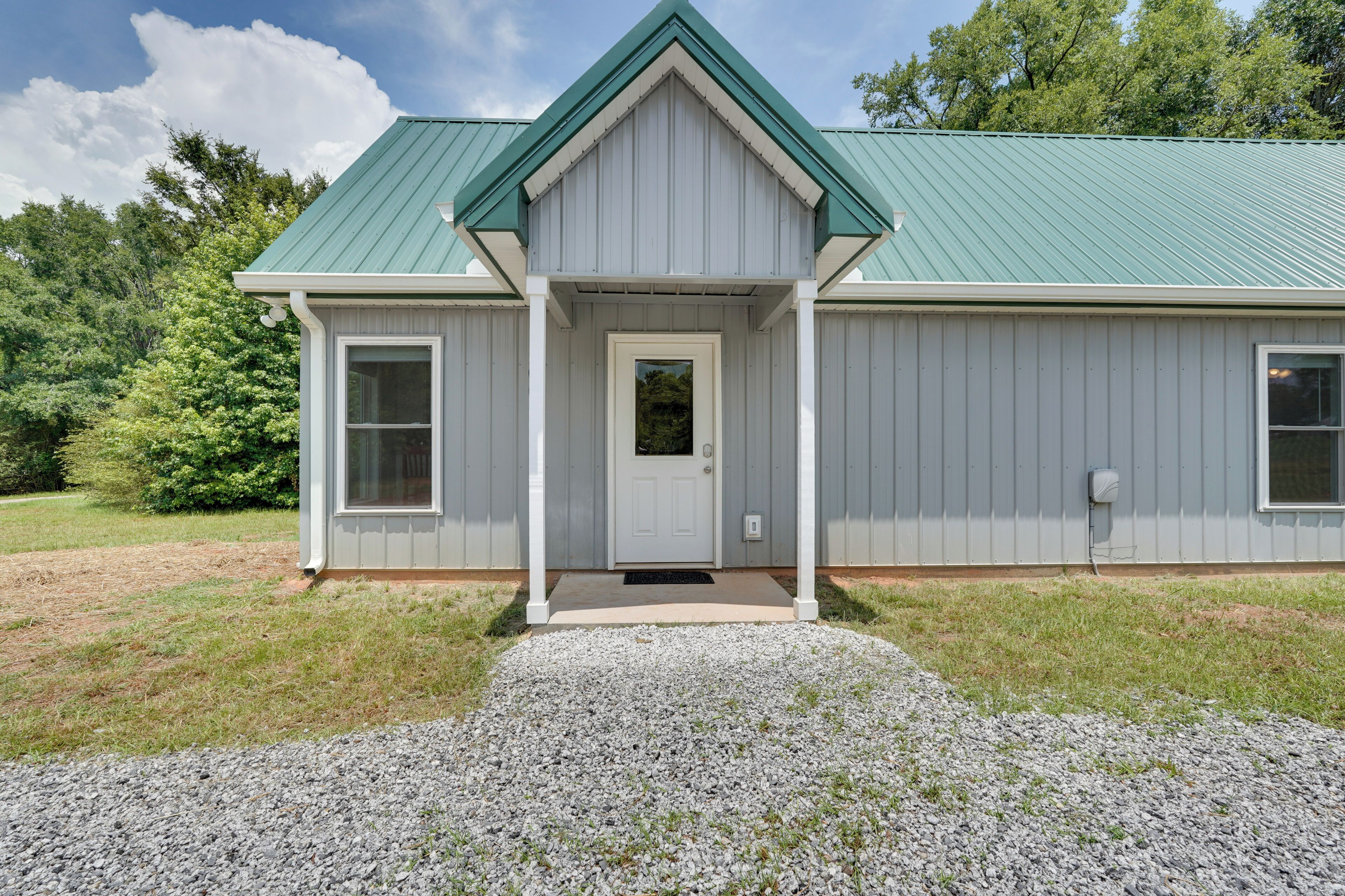 A single-story building with a green roof, a front door, and a gravel driveway.