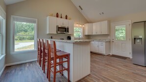 A kitchen with a central island, wooden chairs, white cabinets, a microwave, and a refrigerator. - < 1 Mi to Broad River Campground! Rural Retreat (Tignall)