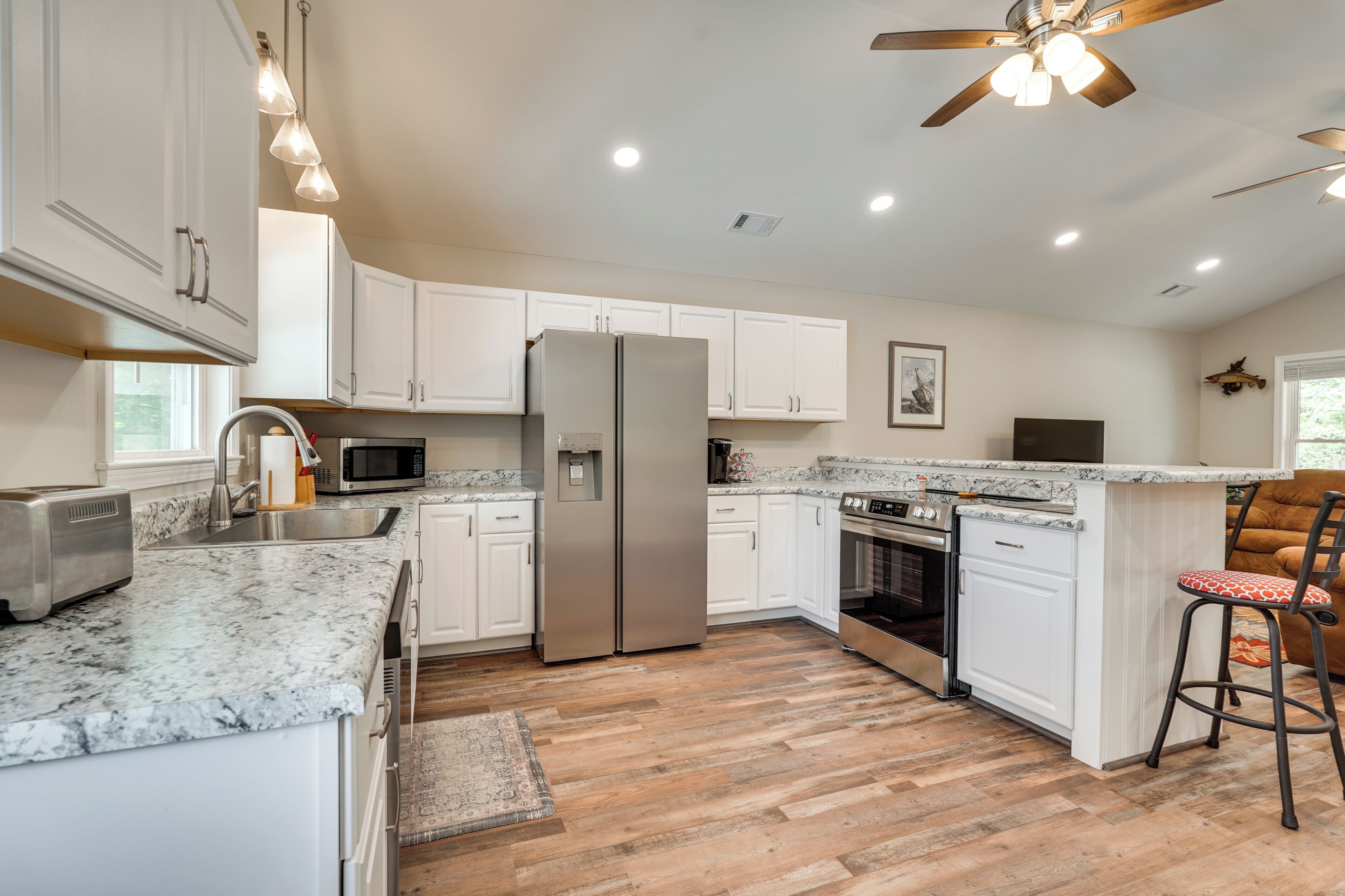 A modern kitchen with white cabinets, stainless steel appliances, a granite countertop, and a ceiling fan.