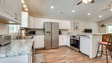 A modern kitchen with white cabinets, stainless steel appliances, a granite countertop, and a ceiling fan.