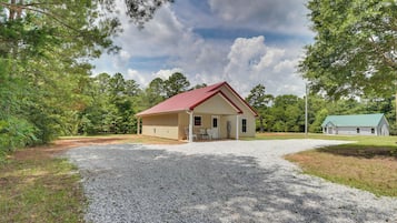 A single-story building with a red roof, a gravel driveway, and a green lawn.