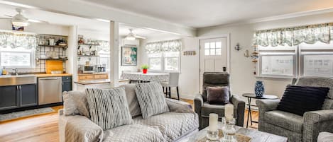 A living room with a sofa, armchairs, a coffee table, and a kitchen in the background.