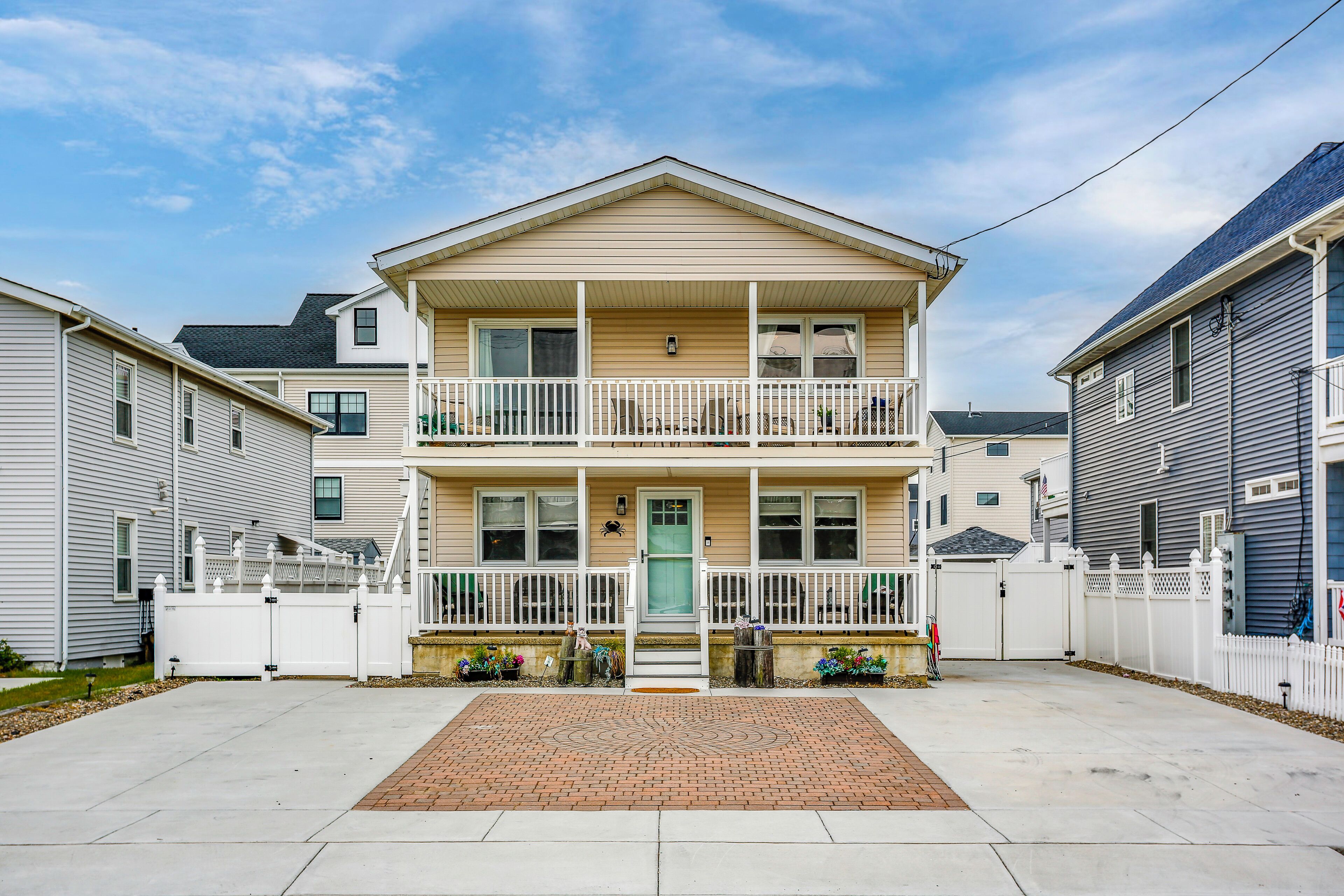 A two-story residential building with a front porch, a gated driveway, and a brick entrance mat.