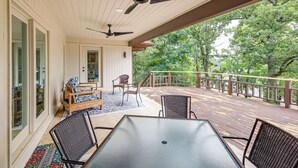 Um deck coberto ao ar livre com mesa e cadeiras, um ventilador de teto e vista para árvores.