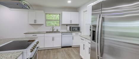 Una cocina moderna con armarios blancos, un refrigerador de acero inoxidable, un microondas y un lavavajillas.