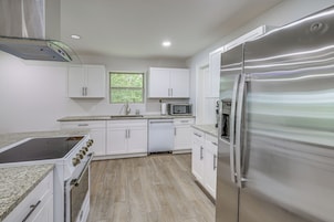 A modern kitchen with white cabinets, a stainless steel refrigerator, a microwave, and a dishwasher.