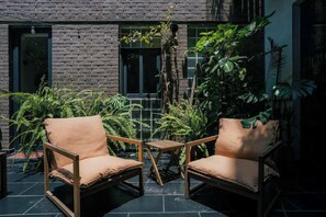 A patio with two wooden chairs and a small table, surrounded by lush green plants and a brick wall. - Escandon Apt: Private Patio & Steps to Condesa (Mexico City)
