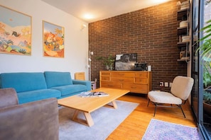 A living room with a blue sofa, wooden coffee table, and a brick wall. - Bright Escandón 2BR | Private Patio Near Condesa (Mexico City)