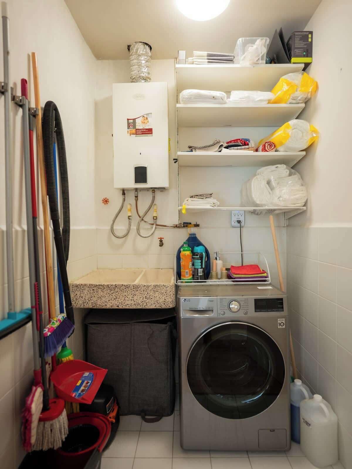 A laundry room with a washing machine, shelves with towels, and cleaning supplies.