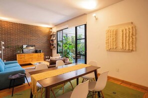 Een moderne leefruimte met een eethoek, een blauwe bank, een houten eettafel en een bakstenen muur.