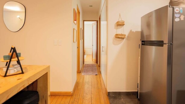 A narrow hallway with a wooden floor leading to a kitchen area with a stainless steel refrigerator. - Escandon Apt: Private Patio & Steps to Condesa (Mexico City)