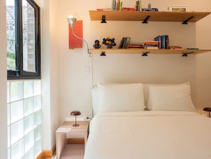 Een slaapkamer met een bed, nachtkastjes, een raam en een boekenkast.
