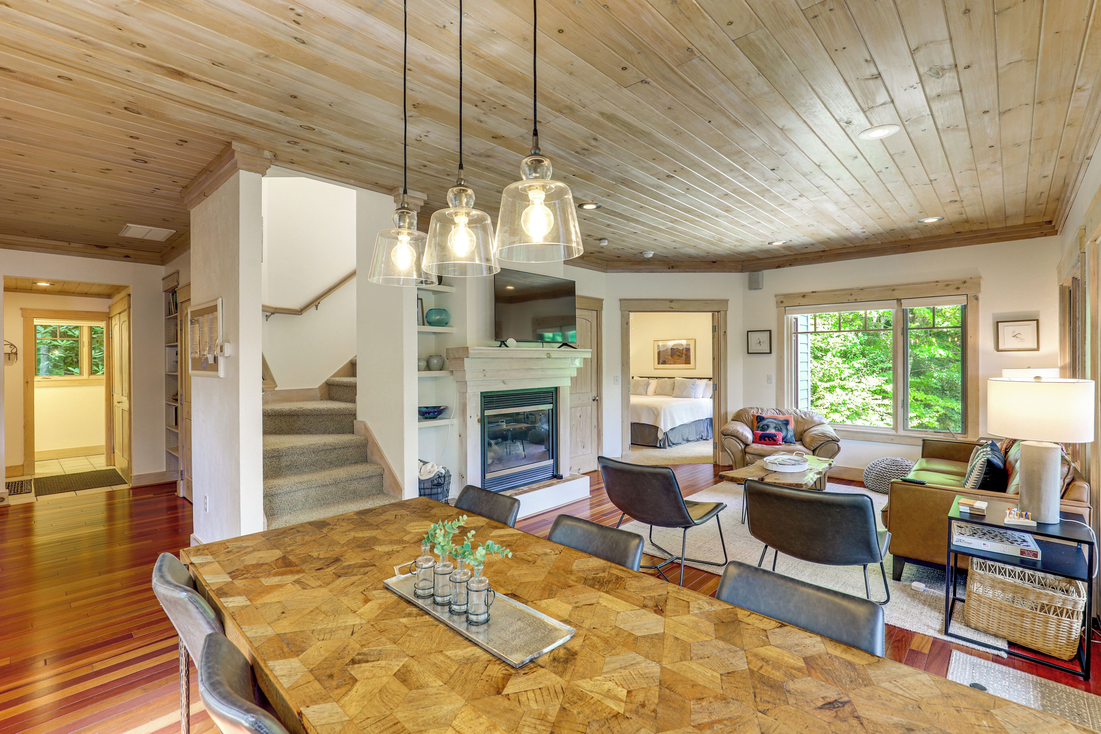 A spacious living area with a wooden ceiling, a dining table with chairs, and a cozy seating area with a sofa and a lamp.