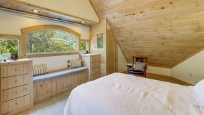 A bedroom with a sloped ceiling, a bed, a bench with storage, a dresser, and a window with a view of trees. - Spacious Home w/ Hot Tub & Views in Black Mountain (Black Mountain)