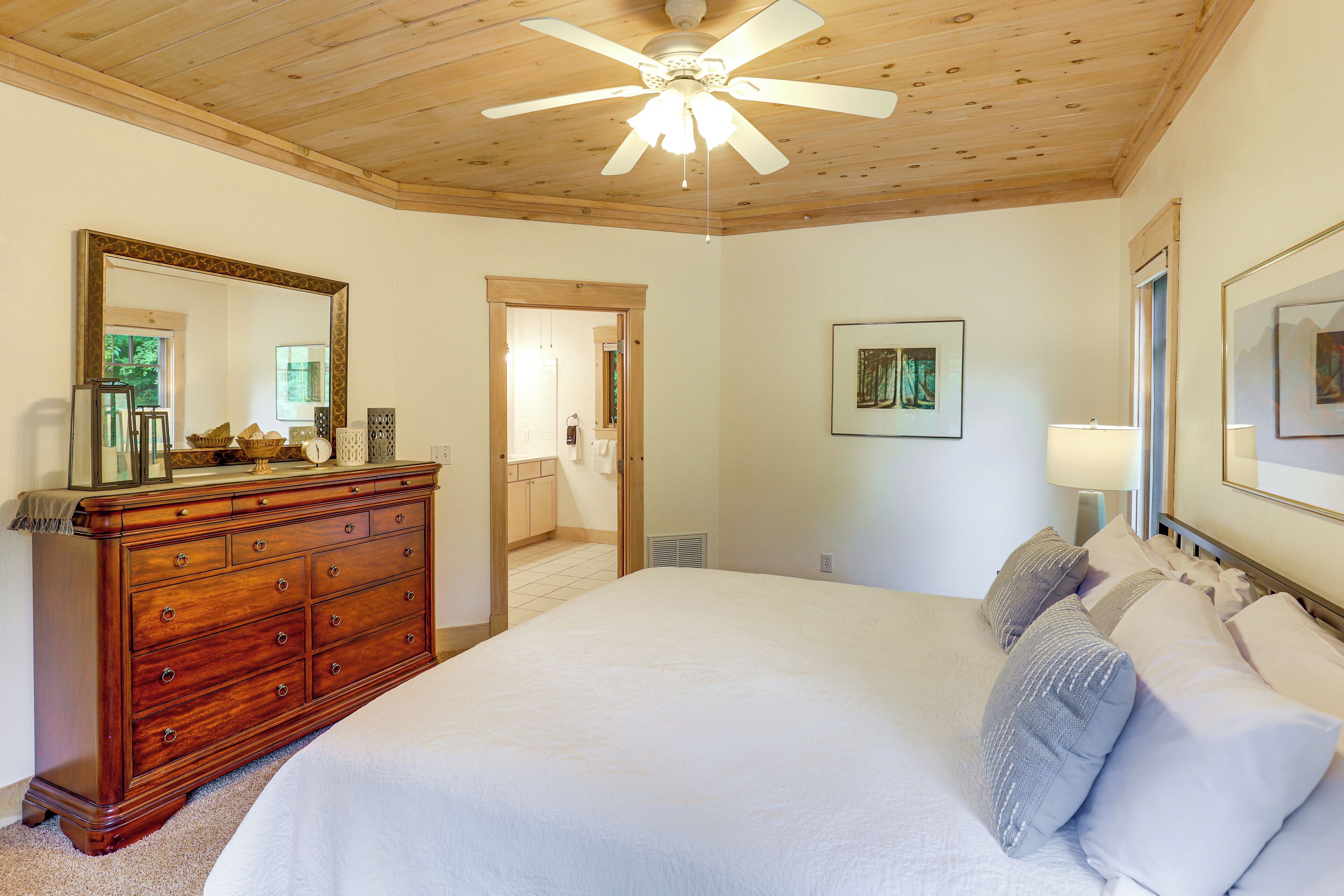 Een slaapkamer met een houten plafond, een groot bed met wit beddengoed, een houten dressoir en een plafondventilator.