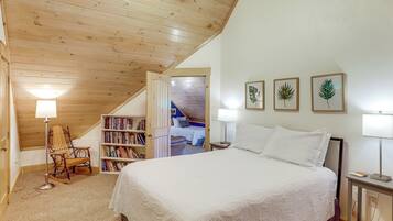 Un dormitorio con techo de madera, cama con ropa de cama blanca, una estantería y grabados botánicos enmarcados en la pared.