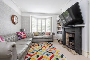 Ein Wohnzimmer mit grauem Sofa, einem farbenfrohen Teppich, einem Kamin und einem Fernseher.
