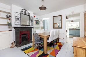 Eine moderne Küche mit weißen Schränken, ein Essbereich mit Holztisch und -stühlen sowie ein farbenfroher geometrischer Teppich.