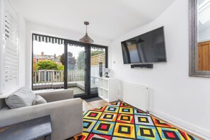 Ein modernes Wohnzimmer mit einer Couch, einem farbenfrohen Teppich, einem Fernseher und einer Glastür zum Balkon.