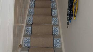 A carpeted staircase with patterned tiles at the bottom, leading to a room with a door and a window.