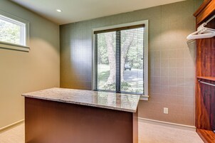 A bathroom with a marble countertop, a window with blinds, a wooden cabinet, and a tiled wall.