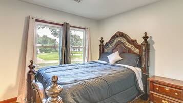 A bedroom with a large bed, a wooden dresser, and a window with curtains.