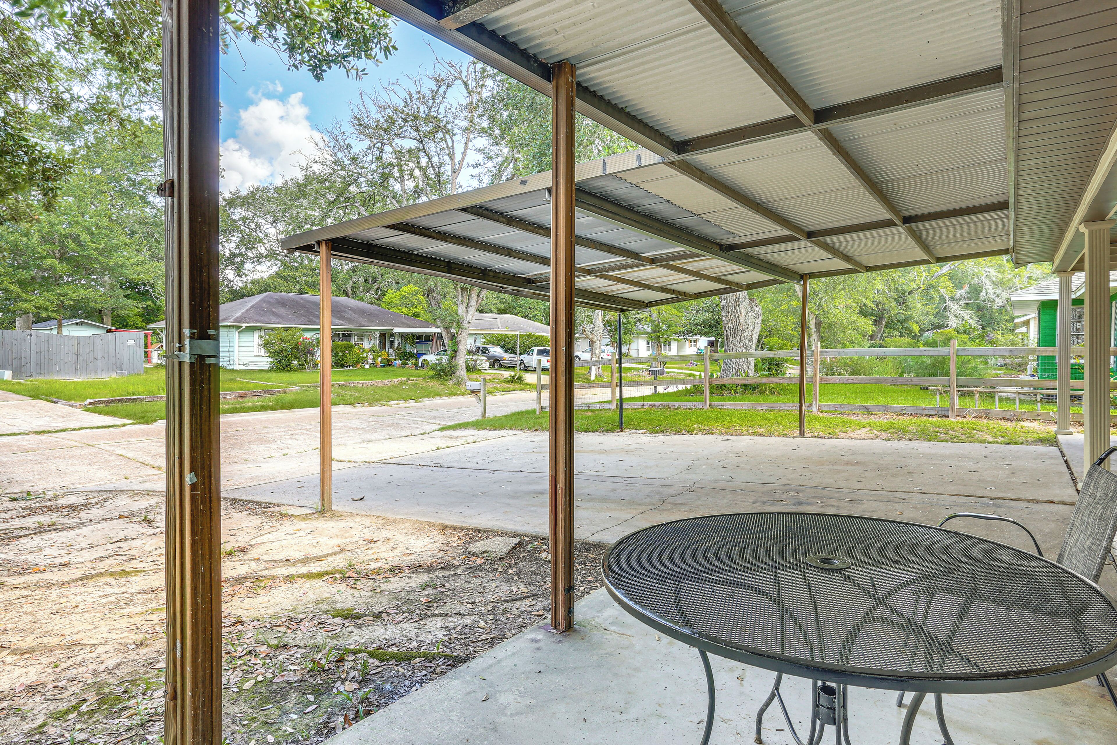 A covered patio area with a metal table and chairs, a concrete floor, and a view of a residential neighborhood.