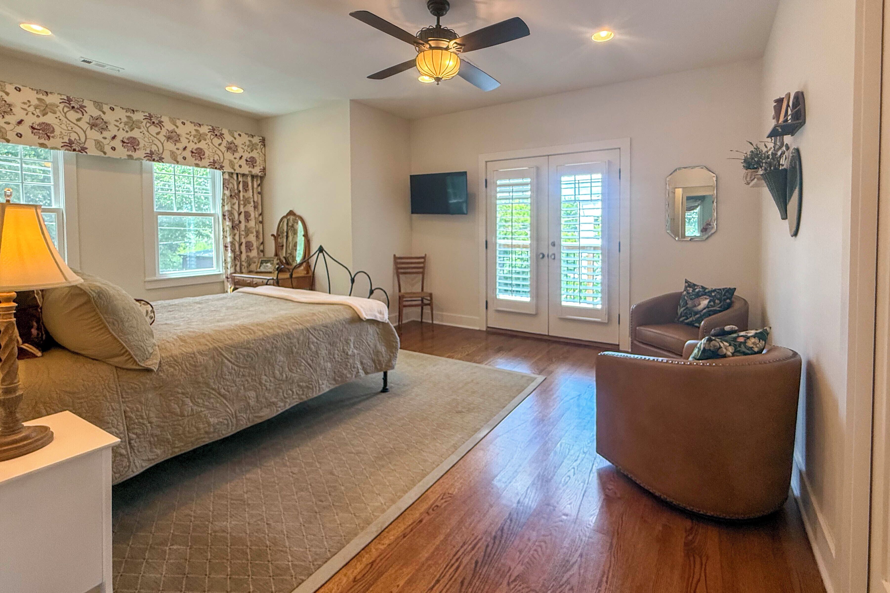 A bedroom with a bed, a chair, a desk, a lamp, a ceiling fan, and a television.